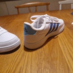 Vita sneakers från Adidas - Snygga vita sneakers från Adidas med klassiska blå ränder på sidan.. Ej använda 