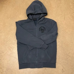 Mörkblå hoodie från Peak Performance - Säljer en snygg mörkblå hoodie från Peak Performance med dragkedja och huva. Perfekt för kyliga dagar. Den har en stilren design med ett tryck på bröstet. Passar bra till både jeans och träningsbyxor.
