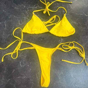 Gul bikini med knytband - Snygg gul bikini med knytband i både över- och underdel. Toppen har trekantsformade kupor och underdelen är designad med smala sidoband för en justerbar passform. Perfekt för soliga dagar på stranden! Bikinin är aldrig använd.