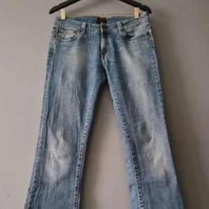 Lowwaist jeans - Snygga blå bootcut jeans med klassisk femficksdesign och knappgylf. Perfekta för en avslappnad stil. De har en lätt tvättad look som ger en vintage känsla.