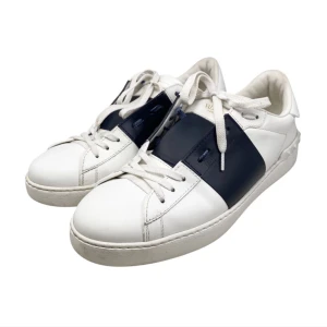 Vit och marinblå Valentino sneakers med nitar - Snygga vita sneakers med marinblå detaljer från Valentino. Skorna har en klassisk snörning och är dekorerade med nitar på hälen för en unik touch. Perfekta för en stilren look.