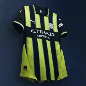 Svart och gul randig fotbollströja från Puma - Snygg fotbollströja från Puma i svart och gul med randigt mönster. Tröjan har korta ärmar och klubbens emblem på bröstet. Perfekt för fotbollsfans som vill visa sitt stöd.