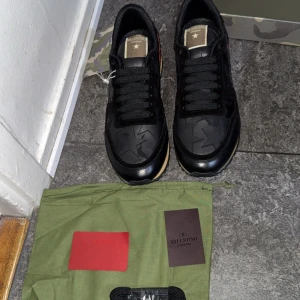 Svarta sneakers från Valentino - Snygga svarta Valentino sneakers med stjärndetaljer och röd häl. Skorna har en unik design med mönstrade paneler och en bekväm sula. Perfekta för att ge din outfit en lyxig touch.