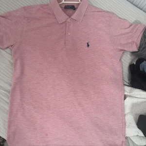 Rosa pikétröja från Ralph Lauren - Säljer en stilren rosa pikétröja från Ralph Lauren med klassisk krage och knappslå. Tröjan har korta ärmar och en liten broderad logotyp på bröstet. Perfekt för en avslappnad men ändå snygg look.