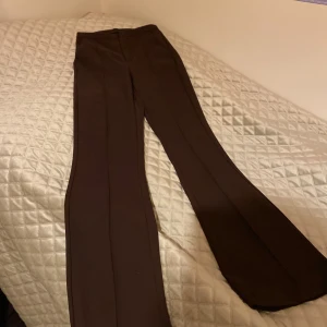 Bruna kostymbyxor från Gina Tricot - Snygga bruna byxor från Gina Tricot i en elegant bootcut-stil. Byxorna har en hög midja och är perfekta för en stilren look. De är tillverkade i ett mjukt material som ger en bekväm passform.