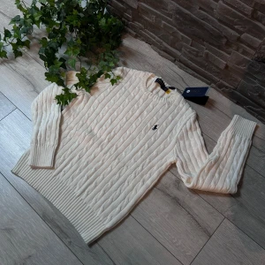 Vit stickad tröja från Ralph Lauren - Säljer en stilren vit stickad tröja från Polo Ralph Lauren. Tröjan har ett klassiskt flätmönster och en broderad logotyp på bröstet. Den är tillverkad i 100% bomull och har långa ärmar med ribbade muddar.