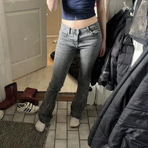 Grå bootcut jeans - Snygga grå bootcut jeans med låg midja. Perfekta för en avslappnad stil. De har en klassisk femficksdesign och en dragkedja med knappstängning.