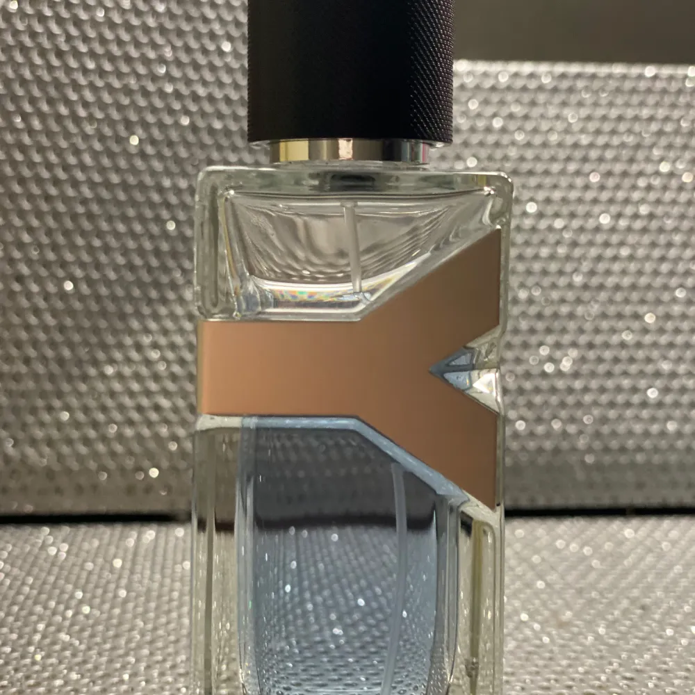 Säljer en elegant herrparfym från Yves Saint Laurent. Flaskan har en stilren design med en fyrkantig form och ett svart lock. Parfymen har en fräsch och maskulin doft som passar perfekt för den moderna mannen. Perfekt för att ge en touch av lyx till vardagen.. Perfume.