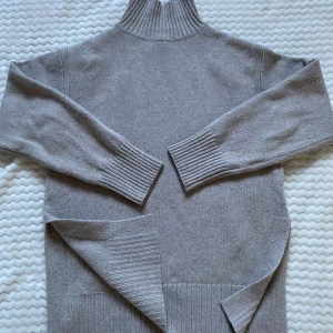 Grå polotröja från H&M  - Säljer en grå stickad polotröja från H&M. Tröjan har en hög krage och långa ärmar med ribbade muddar. Perfekt för kyligare dagar. 64%polyester,30%akryl,6%Ull.  Små noppor finns. 