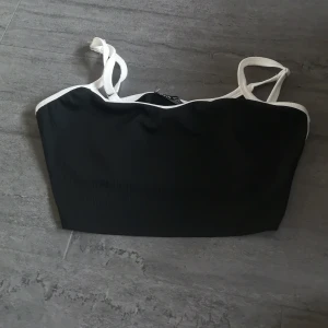 Svart och vit ribbad tubtopp från Shein - Säljer en snygg svart och vit ribbad tubtopp från Shein. Toppen har smala axelband och en kontrasterande vit kant som ger en stilren look. Perfekt för varma dagar eller som ett lager under en jacka.