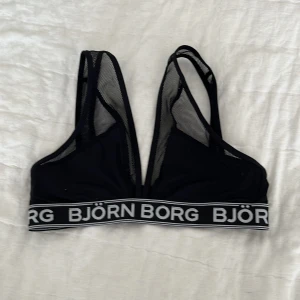 Svart sport-bh från Björn Borg med meshdetaljer - Säljer en svart sport-bh från Björn Borg med bred resår och logga runt om. Bh:n har meshpartier på sidorna och axelbanden för extra ventilation. Stängs med hyska och hake bak. Perfekt för träning eller vardag.