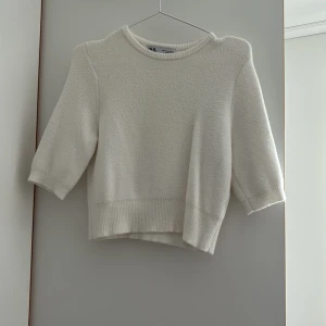 Vit stickad tröja från Zara - Säljer en enkel och stilren vit stickad tröja från Zara. Tröjan har trekvartsärm, rund halsringning och ribbade kant. Använd fåtal gånger, men väldigt mysigt material. 