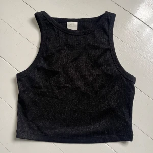 Svart glittrig croppad linnetopp - Säljer en svart glittrig croppad linnetopp från H&M. Toppen har ärmlös design och rund halsringning, perfekt för att lyfta en outfit med lite extra glans. Skriv för fler bilder💞