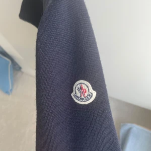 Moncler cardigan - Säljer en mörkblå pufferjacka från Moncler med quiltad front och ärmar i stickad bomull. Jackan har dragkedja framtill och två fickor med dragkedja. Klassisk Moncler-logga på ärmen. Perfekt för kyliga dagar. Nypris 10 000, mitt pris 4499