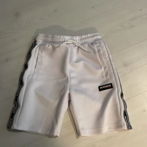 Vita shorts från McKenzie med svarta detaljer - ALDRIG användigt.Snygga vita shorts från McKenzie med svarta logotyper längs sidorna och framtill. Resår i midjan med vit snörning och två sidofickor. Perfekta för en sportig look.