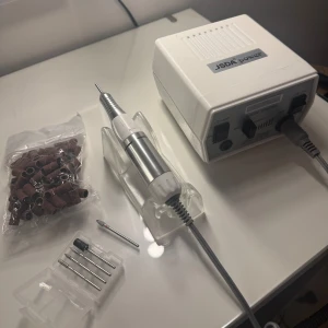 Elektrisk nagelfil med tillbehör - Elektrisk nagelfil från Nagelgiganten. Komplett kit med kontroll enhet, hand stycke och gummiställ. Följer med 4 olika bitsar som kom i kitet + en extra ”hard alloy grinder, small fotball- medium” från NG, nypris: 400kr. Följer även med 80-90st slipningar, ej säker på grit men har för mig att det är 180. Enda som saknas är fotpedalen.