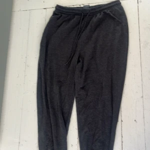 Mörkgrå mjukisbyxor  - Säljer ett par mörkgrå mjukisbyxor med resår i midjan och dragsko. Byxorna har avslappnad passform och muddar vid bensluten. Perfekta för en chill dag hemma eller till träningen.
