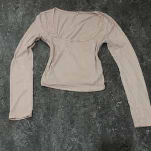 Ljusrosa långärmad topp med rundad urringning - Säljer en ljusrosa långärmad topp med en djup rundad urringning. Toppen är figurnära och tillverkad i ett mjukt, stretchigt material som känns bekvämt mot huden. Tyvärr har tröjan en liten stained smink märke vid V linjen, men går lätt att tvätta bort i tvätten ! 