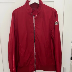 Moncler Windbreaker - Moncler Windbreaker köpt på Moncler för inte så länge sen, äktehets verifierad hos Moncler. Jackan passar perfekt för dom som bär storlek M. Inga tecken på anvdäning jackan är som ny vilket kan ses på bilderna. Annars väldigt sällsynt i just den röda färgen vilket gör att den ger en unik stil. Den köptes från Moncler butiken för 9900. Hör av er om ni har frågor. 