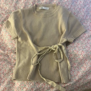 Populär Beige stickad topp med knyt från Zara💗💗 - Säljer en beige stickad topp från Zara med korta ärmar och snyggt knyt i midjan. Tröjan har ribbade detaljer vid ärmslut, hals och nederkant. Perfekt att styla med jeans eller kjol för en trendig look.💗💗