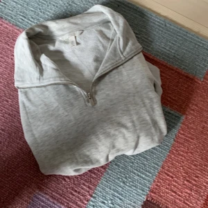 Ljusgrå halvzip tröja från H&M - Ljusgrå tröja från H&M med halv dragkedja och hög krage. Perfekt för en avslappnad stil och enkel att matcha med det mesta. Tillverkad i mjukt bomullsmaterial och har långa ärmar.