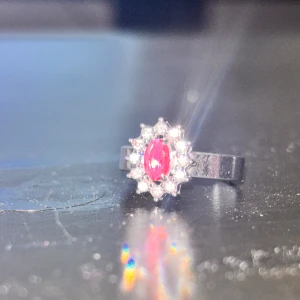 Silverring med röd sten och glittriga stenar - Snygg silverring med en oval röd sten i mitten, omgiven av små glittriga stenar som ger en lyxig känsla. 