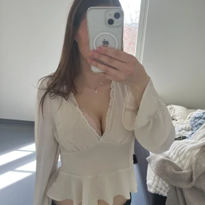 Vit blus med volang och spetsdetaljer - Säljer en söt vit blus med v-ringning och spetskant längs urringningen. Blusen har långa ärmar med volang vid ärmslut