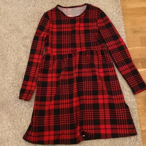 Röd och svart rutig klänning - Säljer en röd och svart rutig klänning med lång ärm och rund halsringning. Klänningen har en lös passform och är perfekt för dig som gillar ett klassiskt rutigt mönster. Bekväm och snygg till många tillfällen.