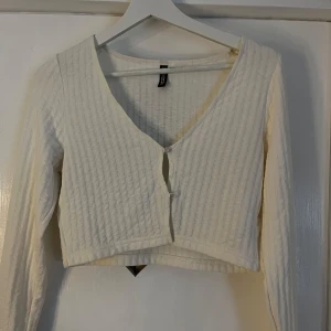 Vit ribbad kofta från H&M Divided - Säljer en vit ribbad kofta från H&M Divided i storlek M. Koftan är croppad med v-ringning och knappar framtill. Långärmad och i mjukt bomullsmaterial, perfekt att styla över ett linne eller t-shirt💗