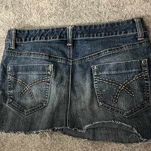 Jeanskjol  - Snygg jeanskjol i blå denim med rå kant och dekorativa bakfickor. Perfekt för en avslappnad stil.