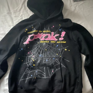 Svart hoodie från Sp5der - Svart hoodie från Sp5der, P!NK tryck. Tröjan är storlek S men passar upp till M. Väldigt gott skick utan tydliga tecken på användning. 