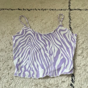 Lila och vit zebramönstrad linnetopp från SHEIN - Säljer en söt linnetopp från SHEIN med lila och vitt zebramönster. Toppen har tunna axelband och är croppad, perfekt för varma dagar. Materialet känns lätt och luftigt.
