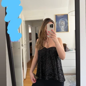Svart glittrig festtopp   - Säljer en svart glittrig bandeau topp med en lätt utsvängd siluett. Den har även silikon vid bysten vilket gör att du inte behöver ha bh under. Aldrig använd. 