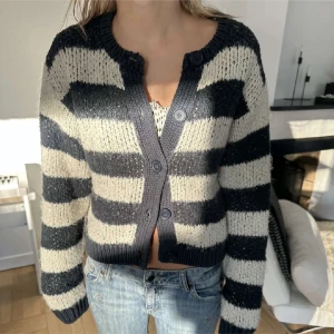 Svartvit randig stickad kofta - Säljer en croppad, stickad kofta med breda svarta och vita ränder. Koftan har långa ärmar, knappar framtill och en mysig, lite oversized passform. Perfekt att slänga över ett linne eller t-shirt.