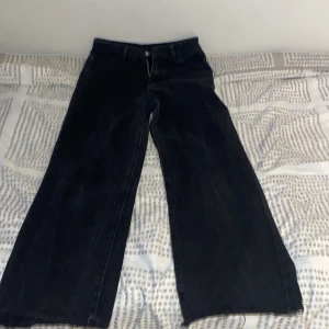 Svarta wide jeans med broderade bakfickor - Säljer ett par svarta jeans med breda ben och snygga broderade detaljer på bakfickorna. Jeansen har normal passform i midjan och stängs med dragkedja och knapp. Perfekta för dig som gillar en trendig och avslappnad stil.
