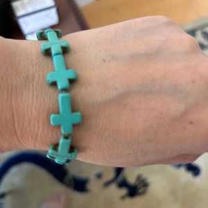 Turkost armband med kors - Säljer ett unikt armband med turkosa korsformade pärlor. Armbandet har elastisk tråd och passar de flesta handleder. Perfekt för dig som gillar färgstarka accessoarer och vill sticka ut.
