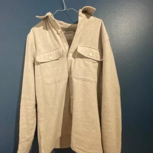Beige overshirt från Jack & Jones - Stilren beige overshirt från Jack & Jones med två stora bröstfickor och knappar framtill. perfekt att bära som lager över en t-shirt. Materialet känns mjukt och har en lätt struktur. Sparsamt andvänd. Passar även S.🫡