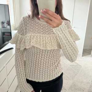 Vit spetsstickad tröja med volang från Lindex - Superfin krämig vit spetsstickad tröja från Lindex med bred volangdetalj över bröstet och långa ärmar. Ny med prislapp 