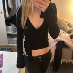 Svart omlottopp med knytband från Gina  - Säljer en svart omlottopp med långa ärmar och knytband i midjan. Från Gina Tricot, använd fåtal gånger.