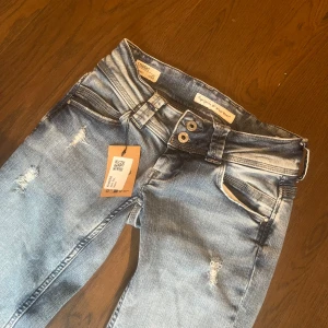 Ljusblå slitna jeans straight low waist - Säljer ett par ljusblå jeans med slitningar och raka ben. Modellen är straight och de är lågmidjade. Jeansen har klassiska fem fickor, dubbla knappar och dragkedja. Perfekta för en avslappnad stil. Sjukt snygga men tyvärr försmå, köpte från Sellpy 💞