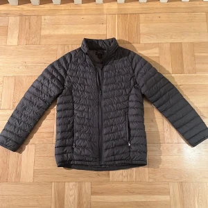 Polo Ralph Lauren Jacka Grå - Detta är en Polo Ralph lauren dunjacka i barnstorleken XL. Den passar som en S/M i manstorlekar och M/L i kvinnostorlekar. Den är i superfint skick. Det enda är att dragkedjan på ena fickan är sönder, men går lätt att laga!  