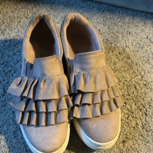 Beige sneakers med volang från Duffy - Säljer ett par beige sneakers från Duffy med dubbla volangdetaljer, super snygga nu inför våren!!