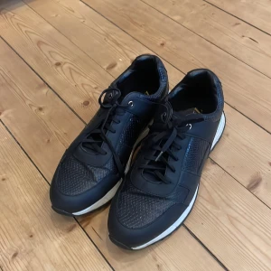 Svarta sneakers från Zara med vita sulor - Säljer ett par svarta sneakers från Zara med snygga detaljer och vit platt sula. Skorna har snörning och inslag av mönstrad textur på vissa partier samt metallfärgade detaljer vid hälen. 