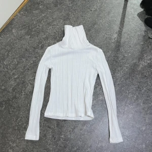 Vit ribbad polotröja från SHEIN - Säljer en vit ribbad polotröja från SHEIN. Tröjan har lång ärm och är tillverkad i ett stretchigt material som sitter snyggt på kroppen. Perfekt att styla med jeans eller kjol för en clean look.
