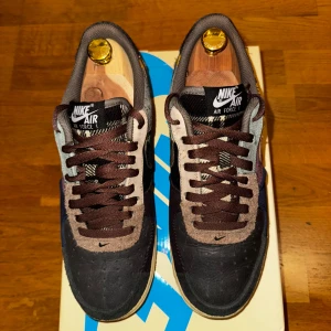 Nike Air Force 1 Travis Scott Cactus Jack - Nike Air Force 1 x Travis Scott ”Cactus Jack” med unik patchwork-design i brunt, svart, grått och beige. Sällsynta och perfekta för dig som vill sticka ut. Original låda + extra snören samt plös medföljer (se sista bild). Storlek eu 41, us 8, uk 7. Sitter lite större i storleken, ish 42. Priset är aningen förhandlingsbart. Vid köp för utropspris ingår ett par crease protectors (se sista bild). 