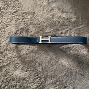 H bälte - Snyggt blått skärp från H med det ikoniska H-spännet i silverfärg. Bältet är gjort i slätt skinn med vita sömmar längs kanterna och har en stilren, klassisk design som verkligen sticker ut.