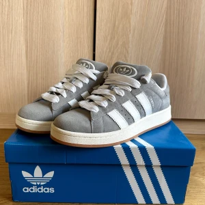 Adidas Campus 00s  - Snygga Adidas Campus sneakers i grå mocka med klassiska vita ränder och vit sula. Skorna har rund tå, platt sula och vita skosnören. Använda 1 gång men var för stora för mig