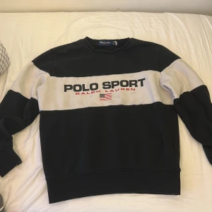 Polo Sport tröja svart/vit Ralph Lauren - Snygg svart och vit tröja från Polo Sport Ralph Lauren med breda blockränder och stor logga framtill. Klassisk crewneck-modell med långa ärmar och mjukt material. Perfekt för dig som gillar sportig och stilren streetwear. 