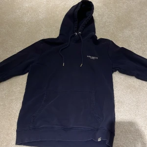 Mörkblå hoodie från Les Deux - Snygg mörkblå hoodie från Les Deux med broderad logga på bröstet. Klassisk känguruficka framtill, justerbar huva med snörning och ribbade muddar. Perfekt för en chill och stilren look.