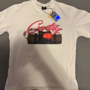 Vit t-shirt Adygatic NO TIME 4 LUV XL - Vit t-shirt från Adygatic i bomull med tryck av en bomb och rosa graffiti på framsidan samt stor svart text 'NO TIME 4 LUV' på ryggen. Klassisk passform och rund hals. Perfekt statement-plagg för dig som vill sticka ut.